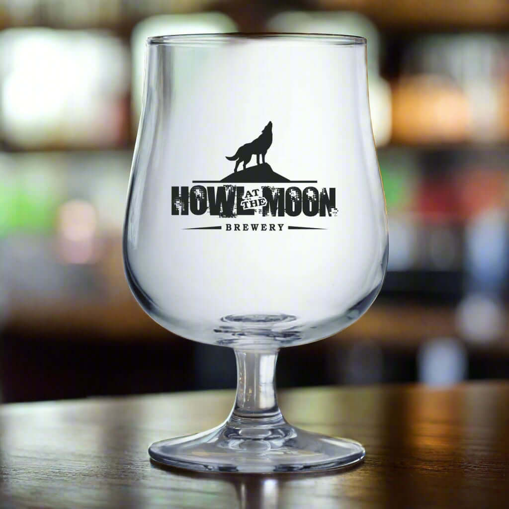 Custom Arc 16.75 oz Belgium craft beer glass with Howl at the Moon Brewery logo on a wooden table.